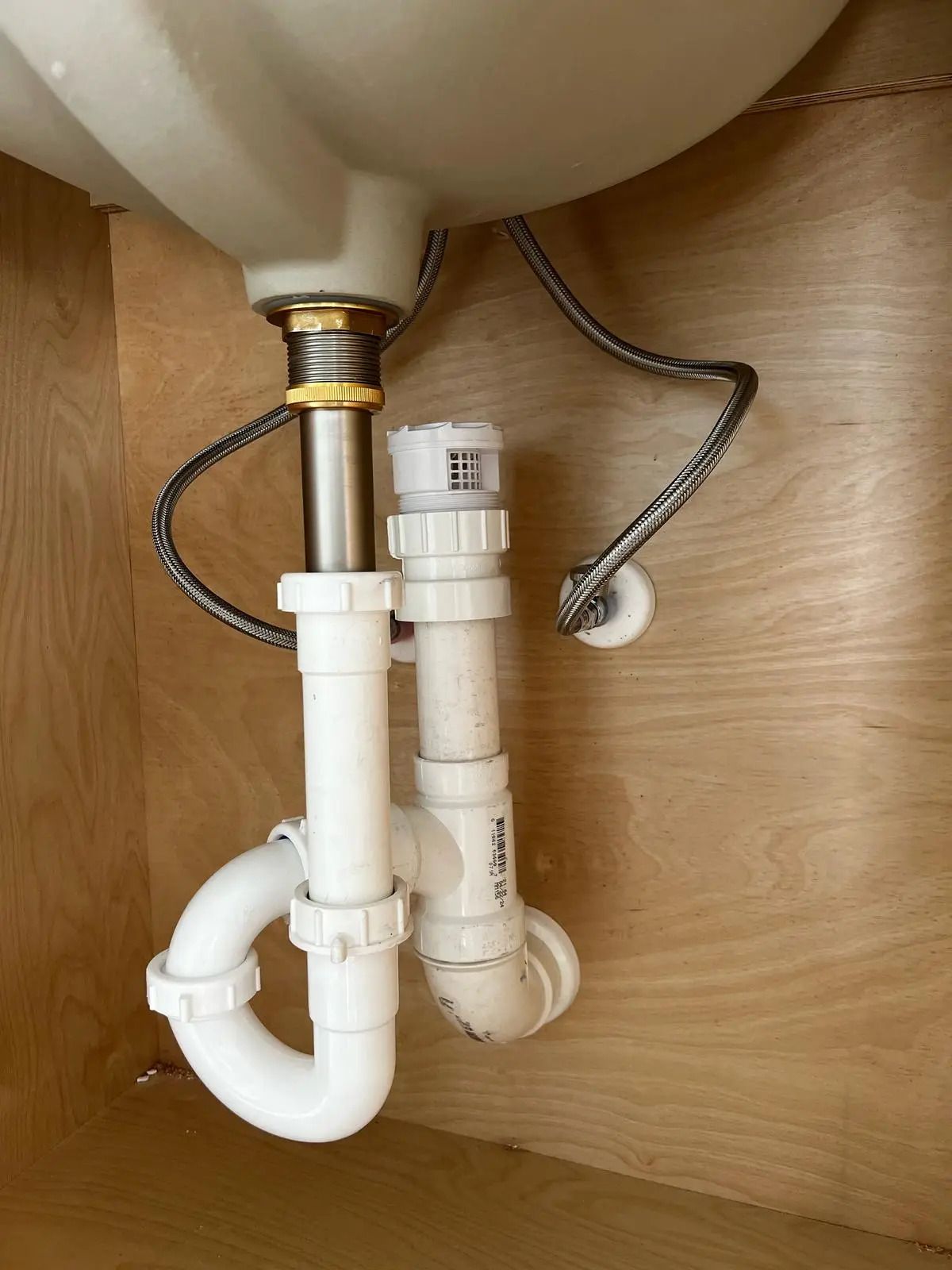 PVC P-trap, drain and braided water supply lines under a bathroom sink