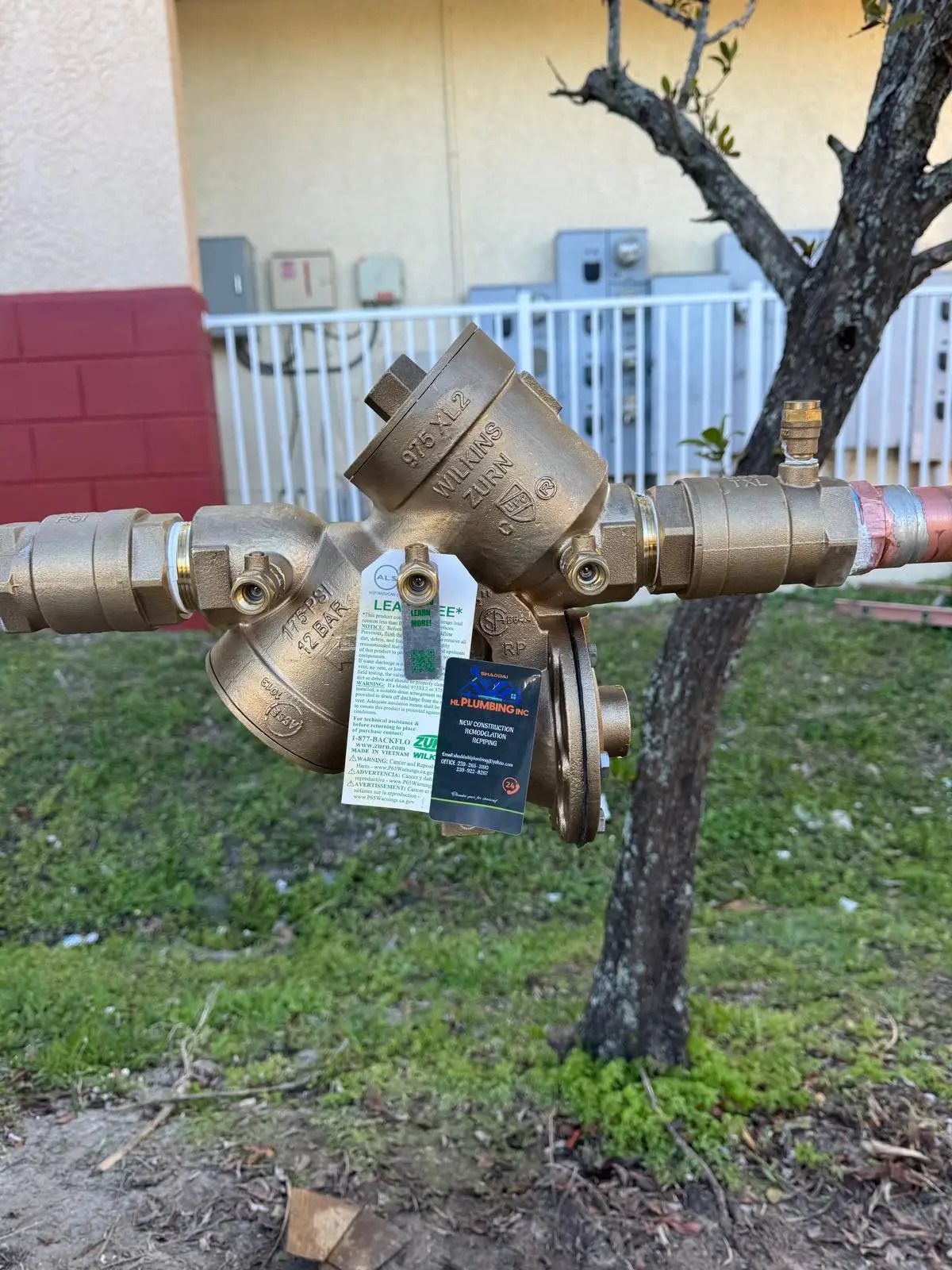 Close-up of a brass backflow preventer with a Shaddai HL Plumbing test tag