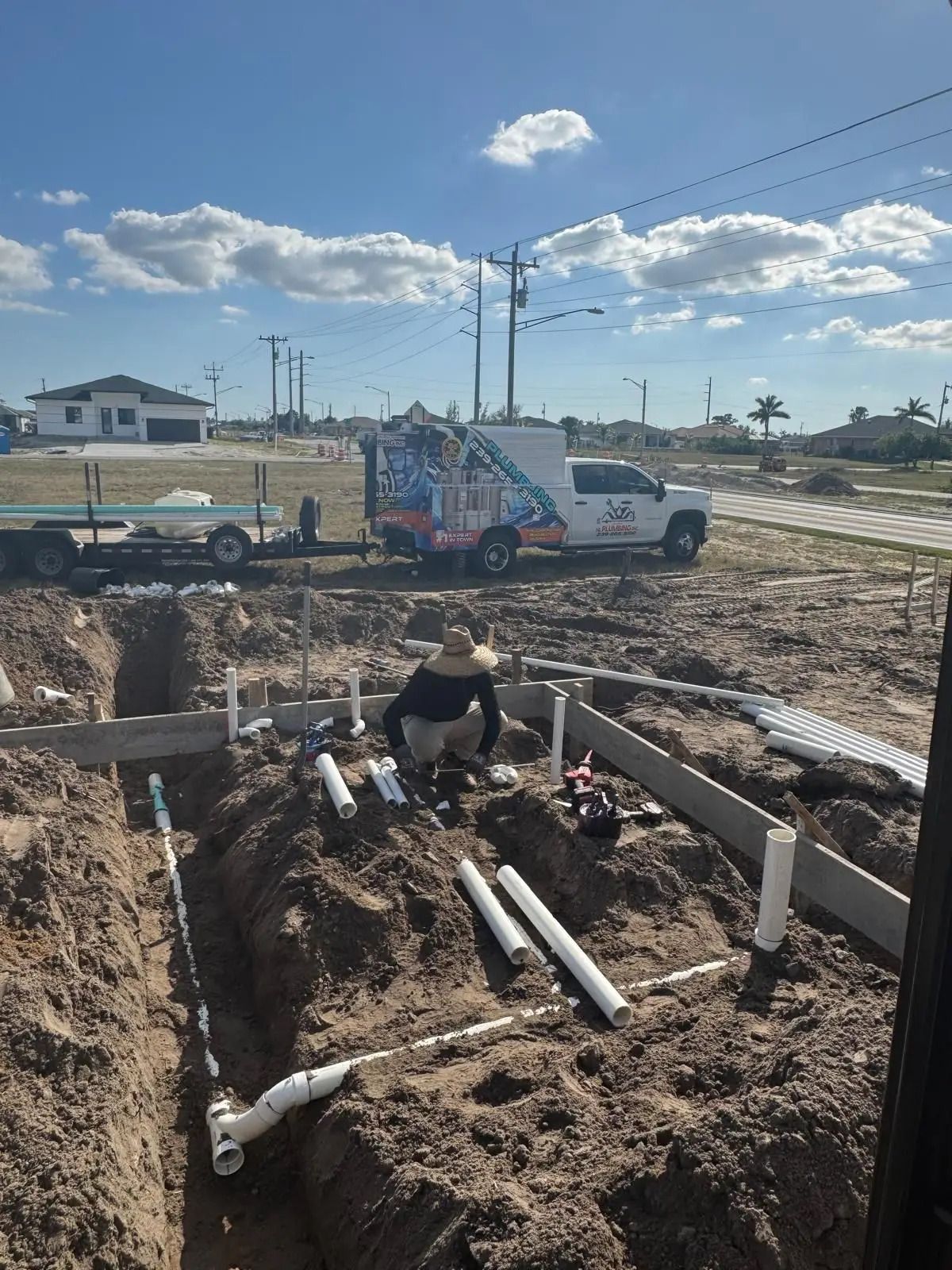 Plumber laying out underground PVC drain lines in trenches before a slab pour