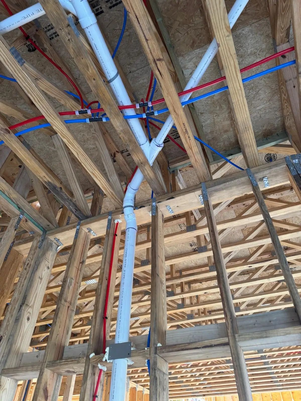 PVC drain stack and red and blue PEX water lines run through framing and trusses