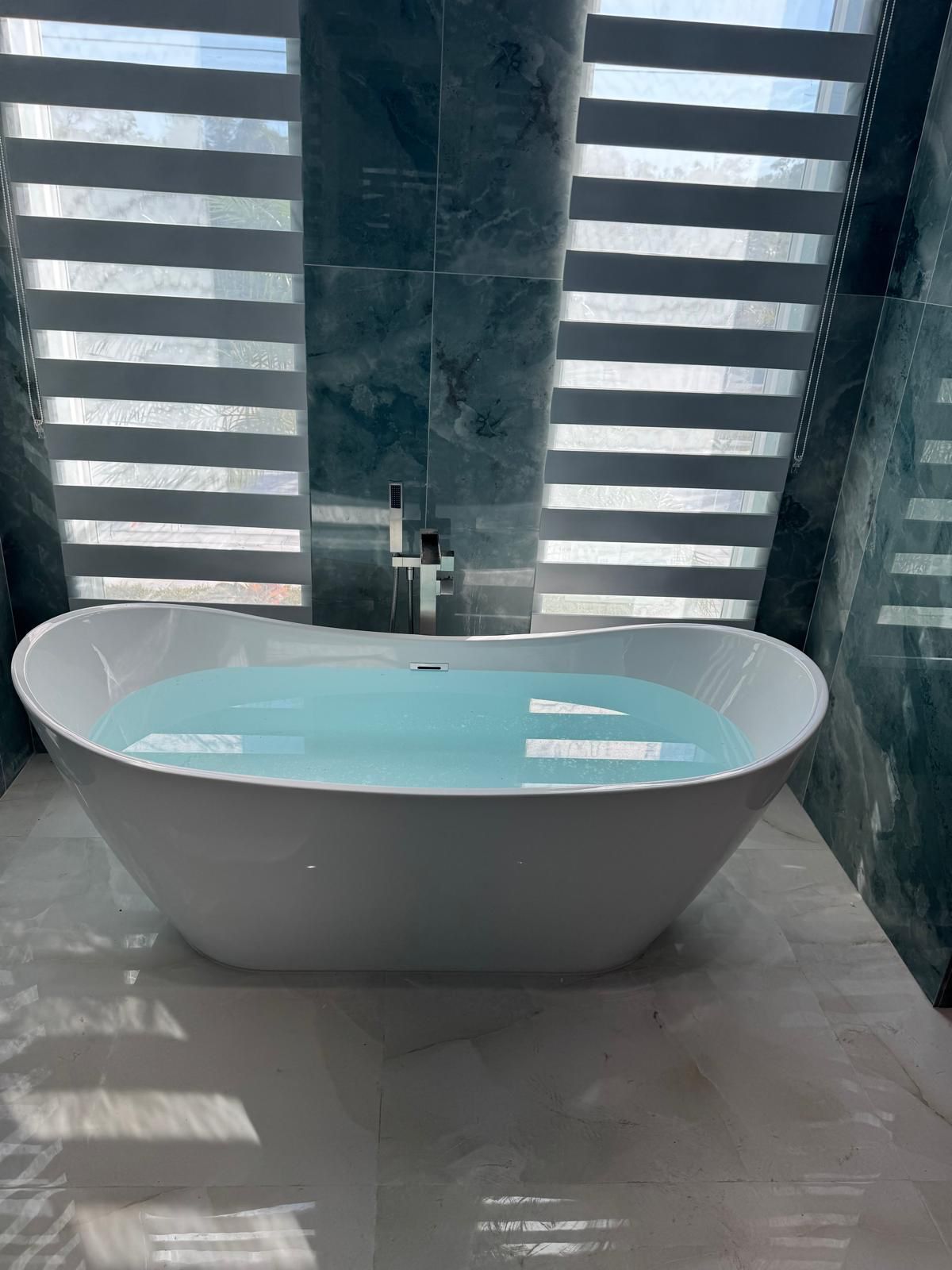 White freestanding soaking tub filled with water beside a floor-mounted tub filler